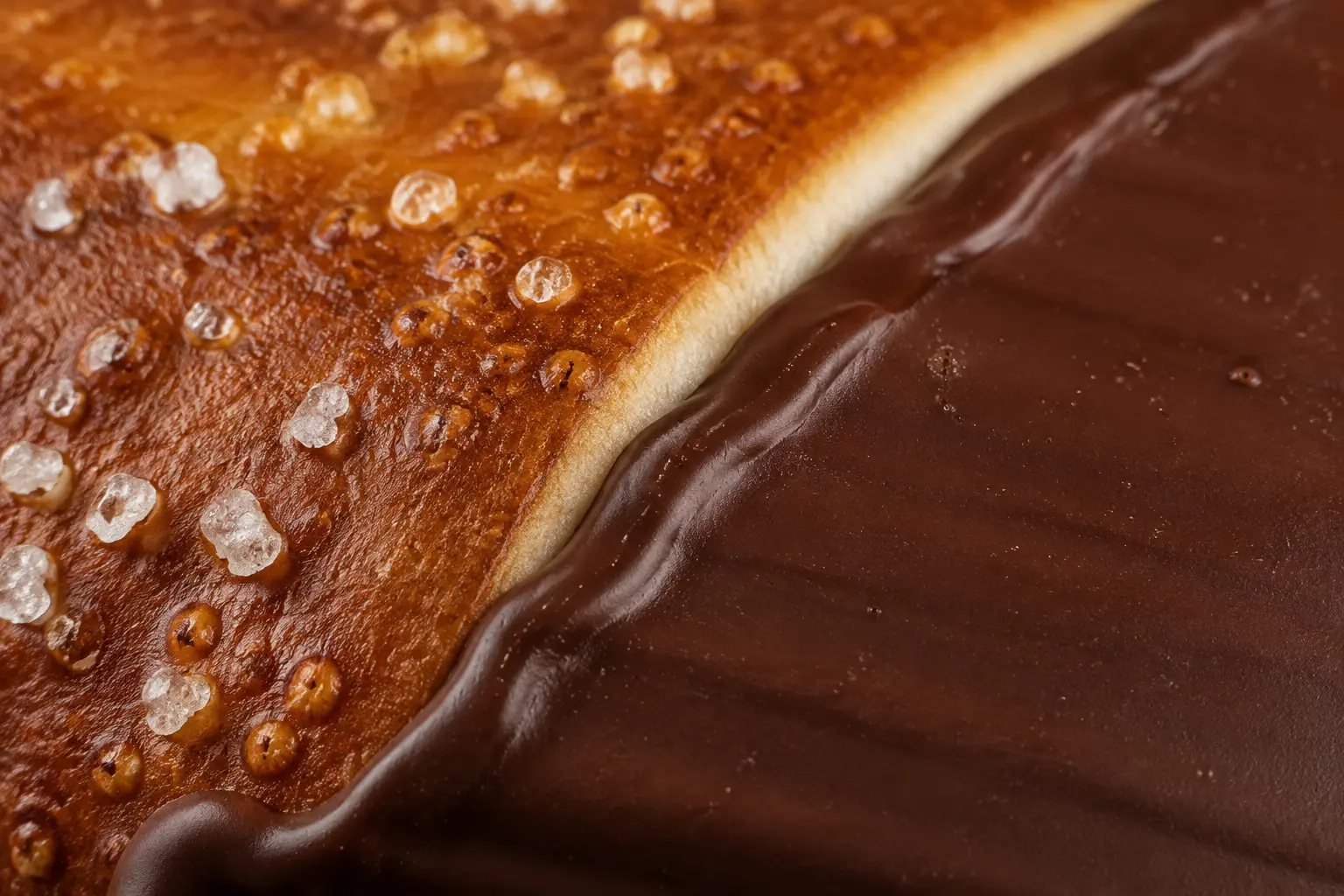 Extreme macro of the real meeting point between salted baked pretzel crust and glossy dark chocolate